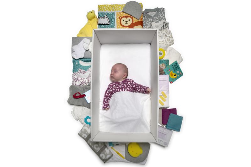 Scotland's baby box containing baby clothes, a blanket, a bath towel and a baby wrap, toys, bibs, a digital underarm thermometer and nursing pads